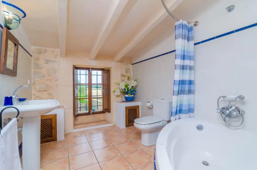 Un baño con suelo de baldosas, bañera, cortina de ducha, lavabo y ventana.