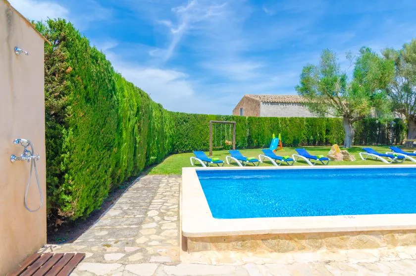 Una piscina al aire libre junto a un sendero de piedra y setos verdes.