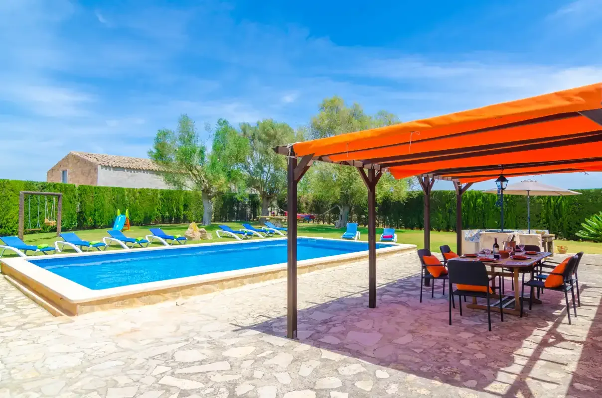 Una piscina exterior junto a una zona de comedor con sombra, mesa y sillas.