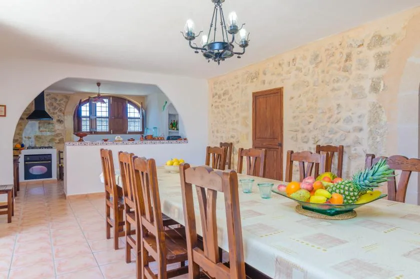 Comedor con una mesa larga preparada con fruta y vasos junto a una abertura arqueada hacia la cocina.