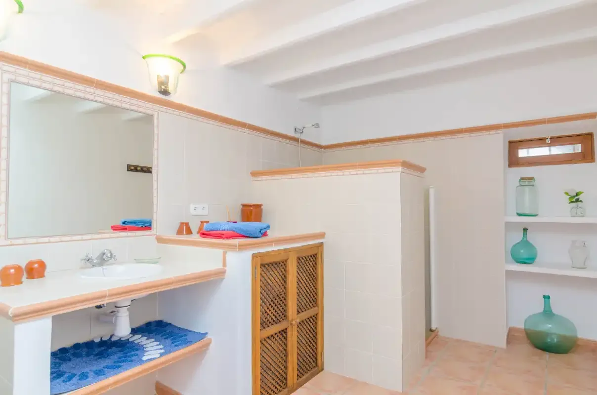 Un baño luminoso con un largo lavabo, un espejo grande y una zona de ducha alicatada.