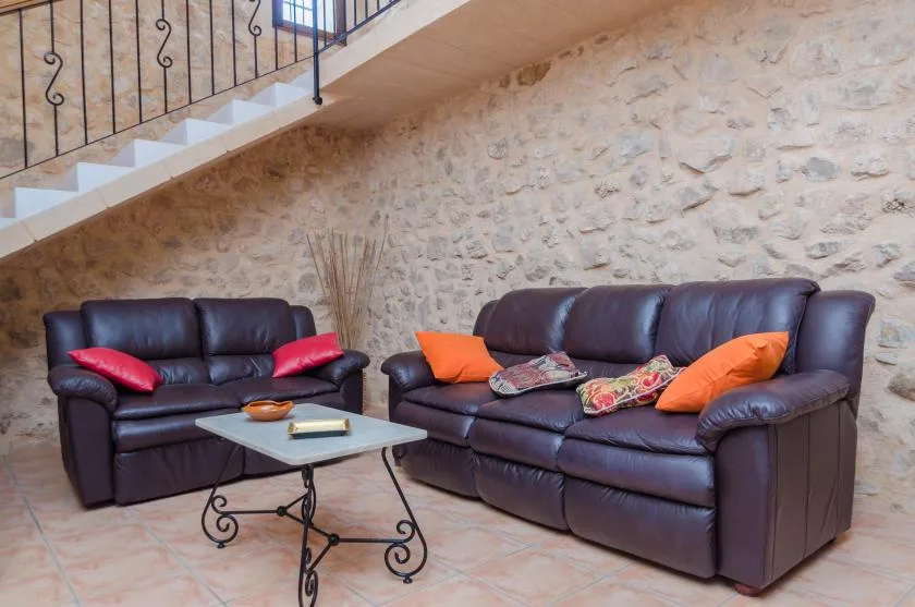 Una zona de estar con sofás de cuero oscuro, cojines coloridos y una mesa de centro.