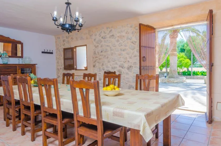 Un comedor con una mesa larga y asientos de madera junto a una puerta abierta.