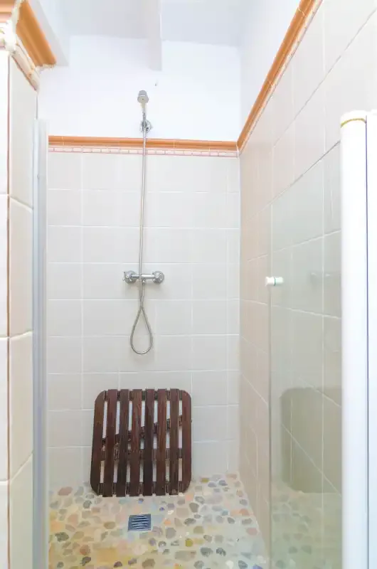 Una ducha alicatada con rociador de pared y suelo de dibujo de guijarros.