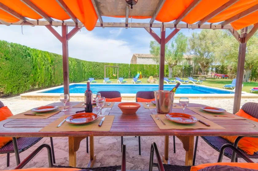 An outdoor dining table sits beneath an orange canopy beside a swimming pool.