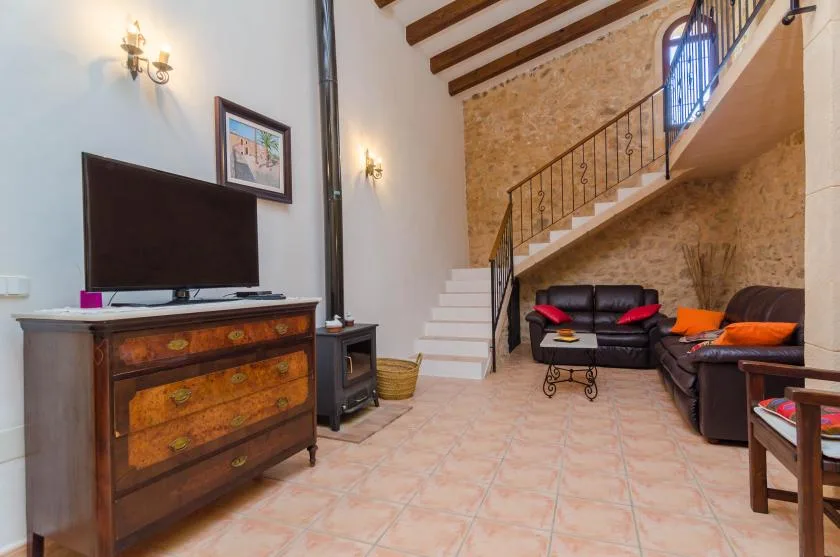 Una sala de estar con asientos oscuros, un televisor y una escalera.