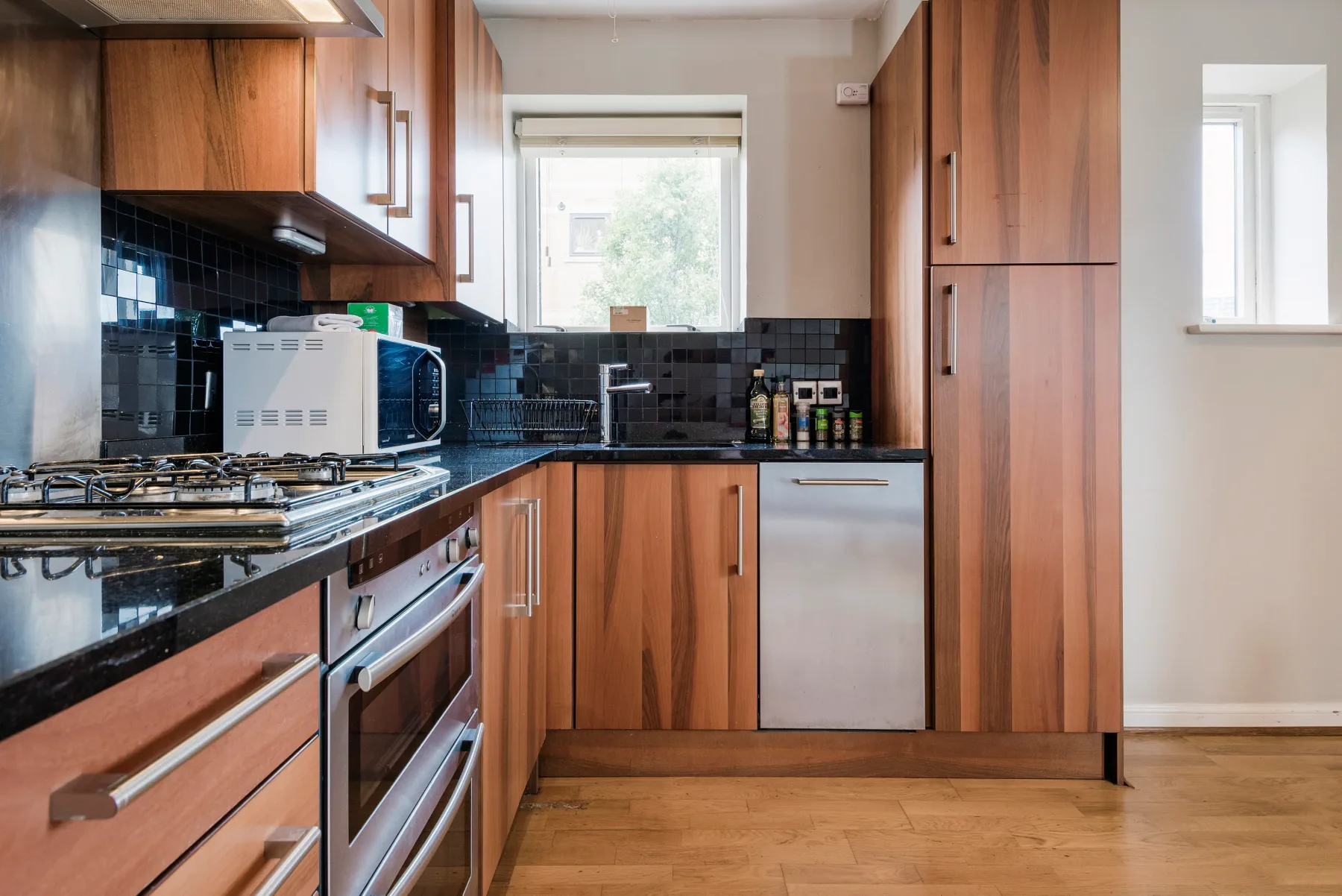 A kitchen with wood cabinetry, dark countertops, and a window above the sink.