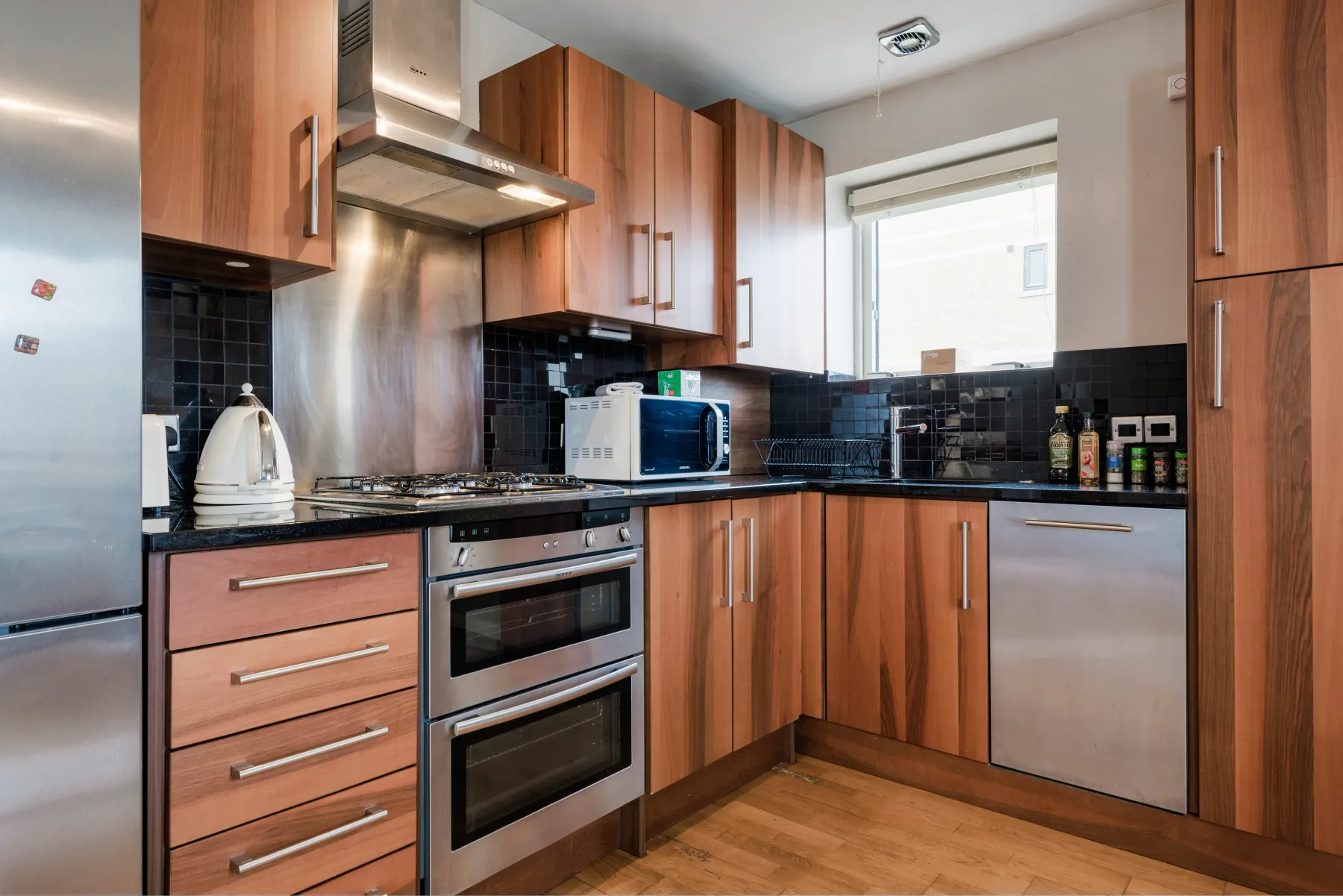 A kitchen with wooden cabinets, black tile backsplash, and stainless steel appliances.