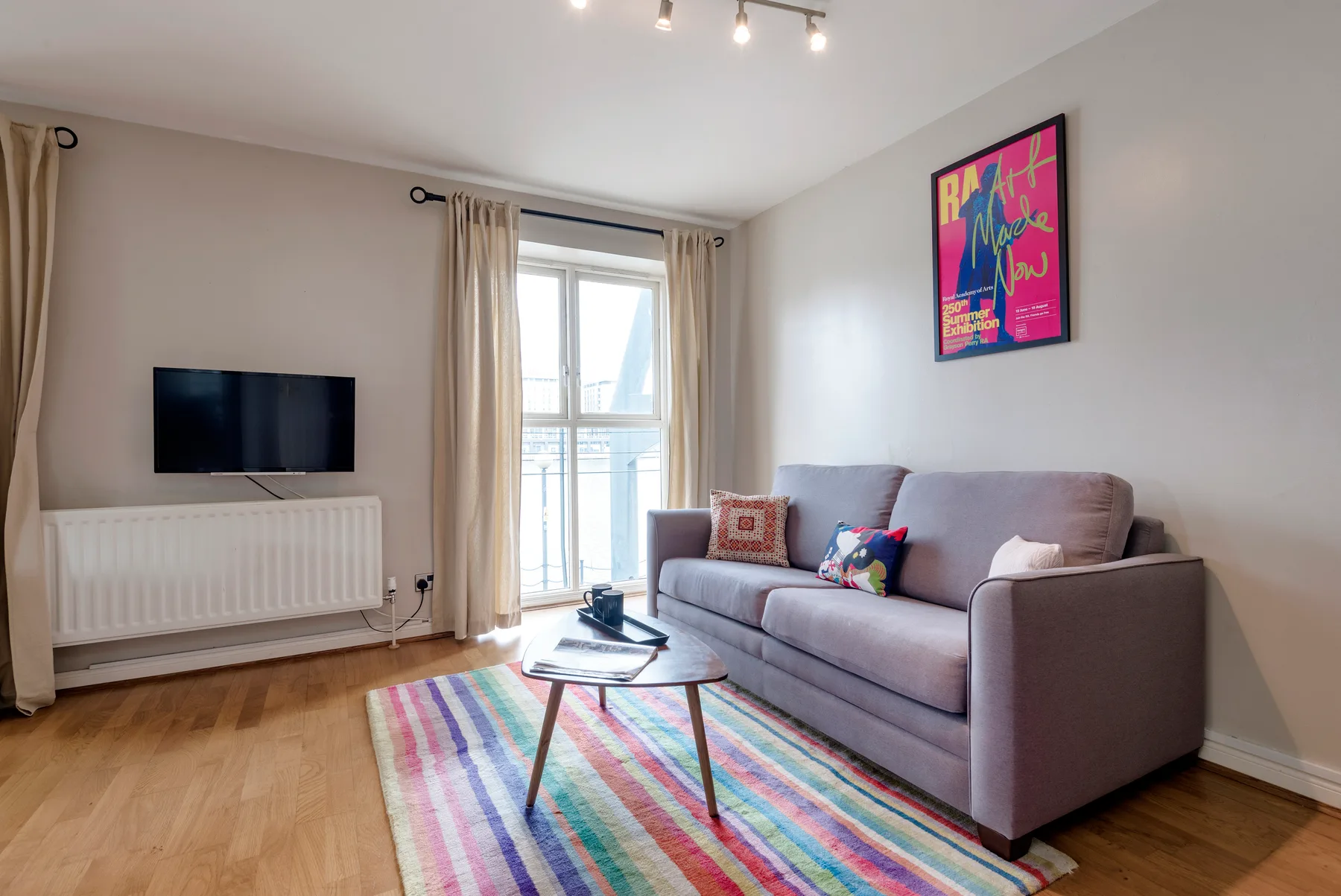 A bright living room with a sofa, television, and colorful striped rug.