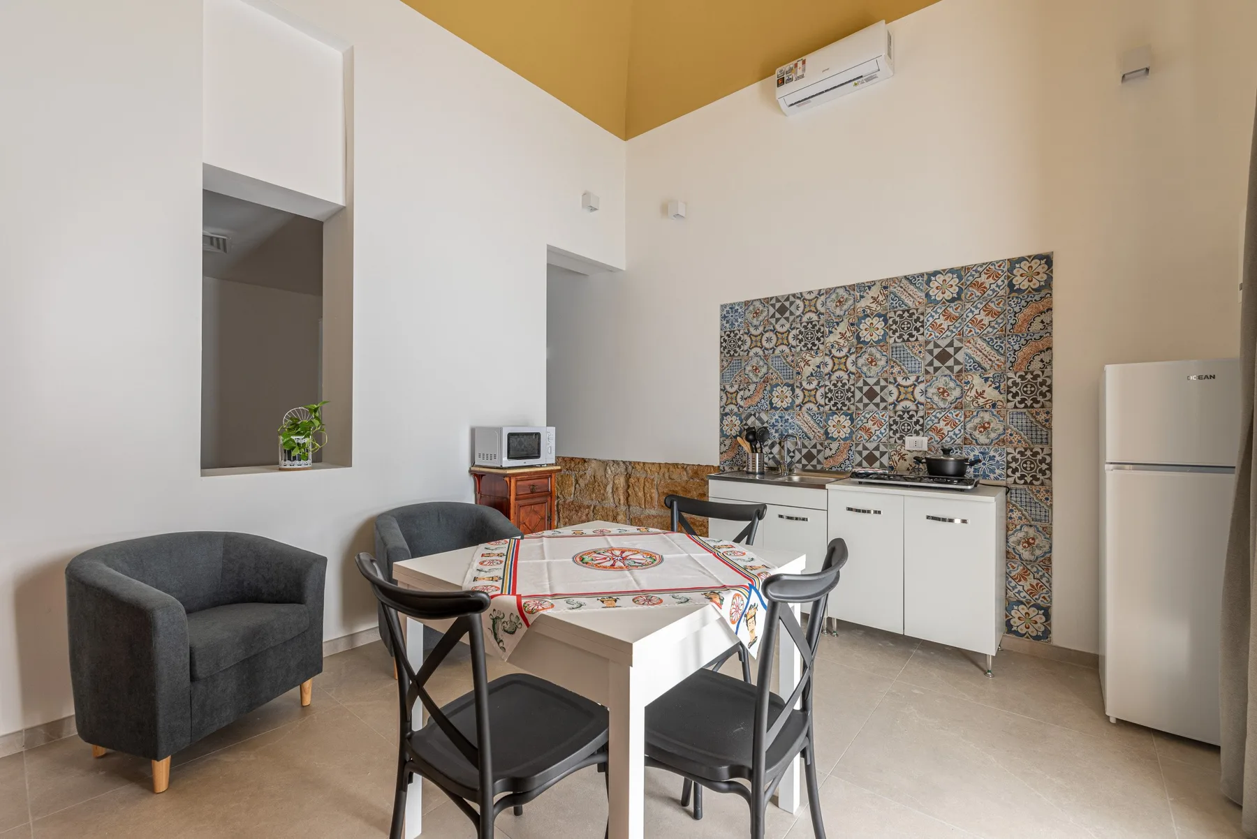 A dining area with a table and seating beside a kitchen with patterned backsplash.