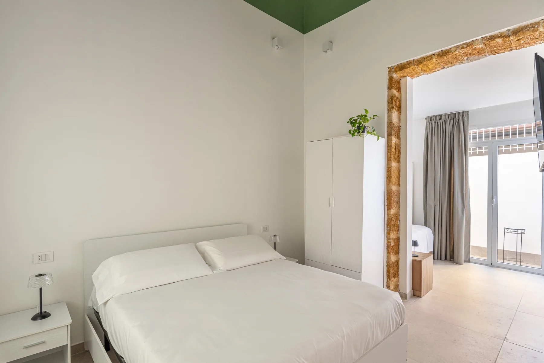 Un dormitorio luminoso con una cama tendida y una puerta abierta hacia una zona de estar.