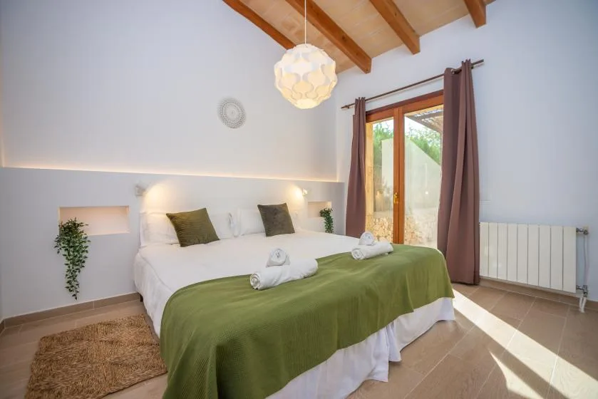 Un dormitorio luminoso con una cama cubierta por una manta verde y una ventana alta.