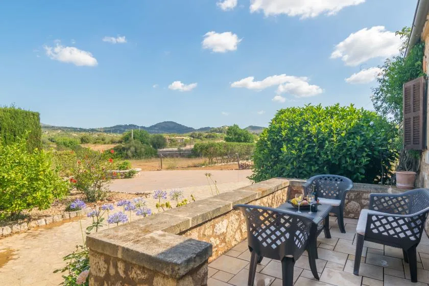 Un patio exterior con asientos da a un jardín y colinas lejanas.