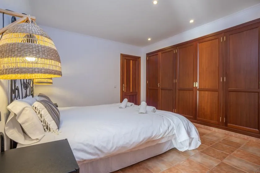 Un dormitorio con una cama, una lámpara colgante tejida y armarios de madera.