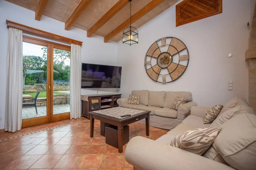 Una sala luminosa con asientos beige, un televisor y vigas de madera expuestas en el techo.