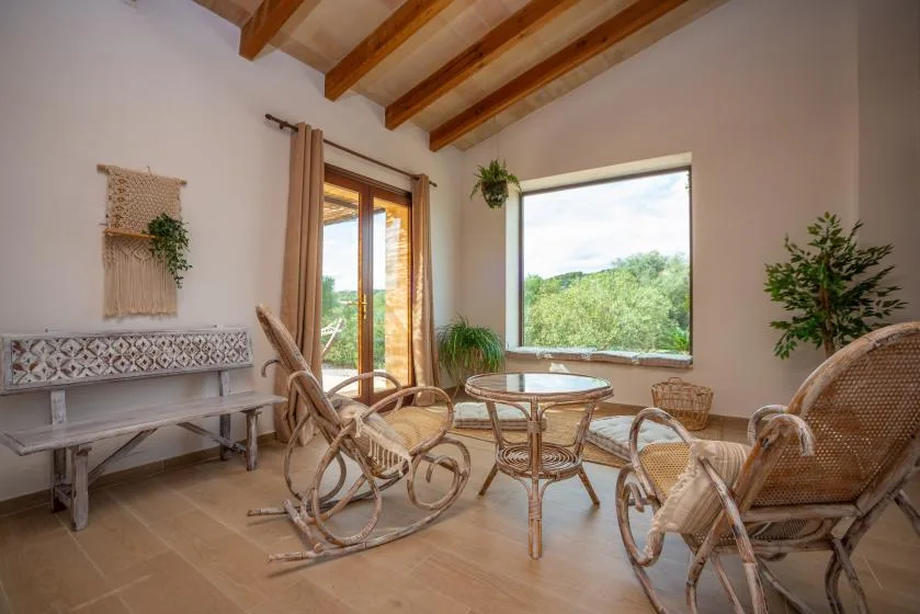 Una luminosa sala de estar con asientos tejidos, una mesa de vidrio y grandes ventanas.