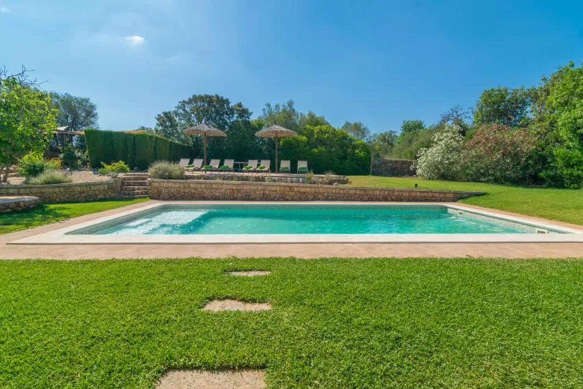 Una piscina al aire libre junto a un césped y setos de jardín.