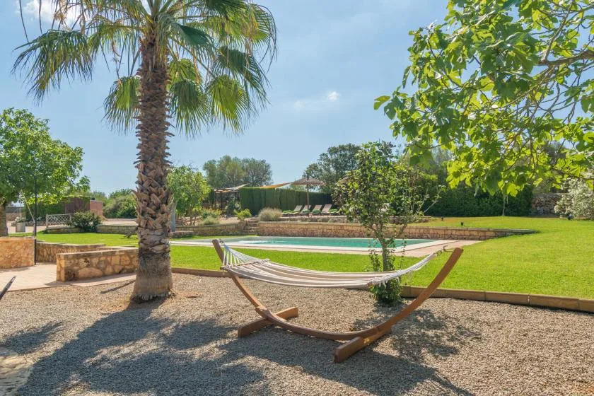 Una hamaca cuelga junto a una piscina en un jardín soleado.