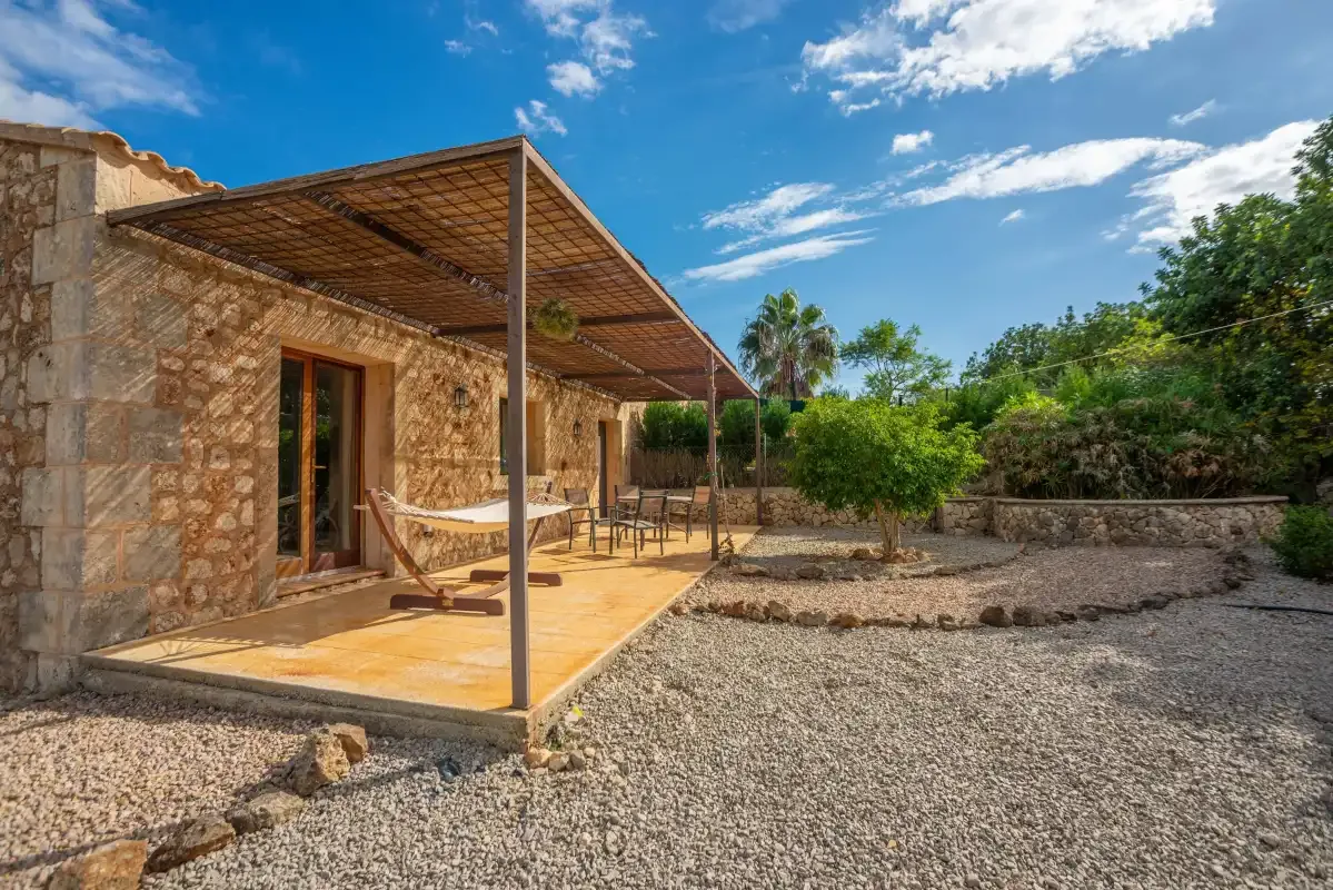 Una casa de piedra da a un patio sombreado con asientos al aire libre y un jardín de grava.