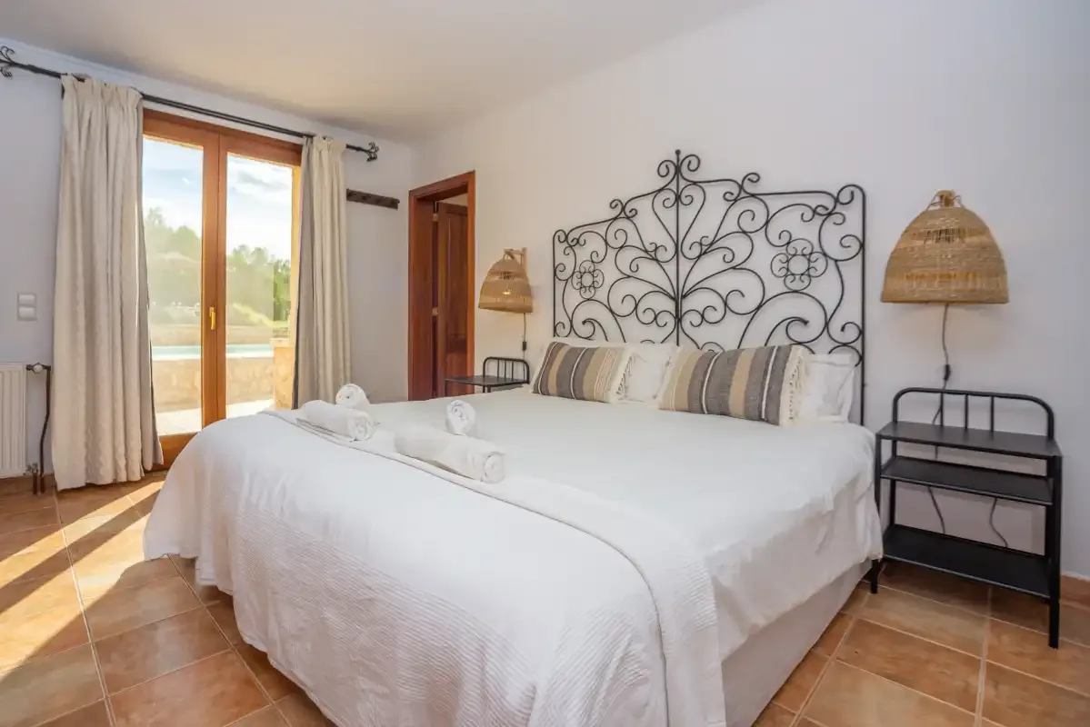 Un dormitorio con una cama grande, cabecero metálico decorado y puertas acristaladas a un patio.