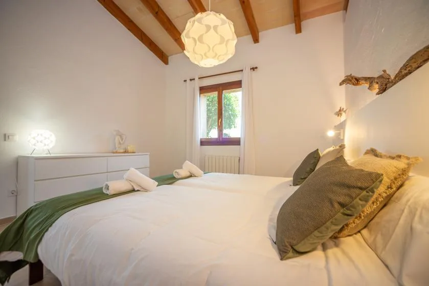 Un dormitorio con una cama bien arreglada y una ventana bajo vigas de madera vistas.