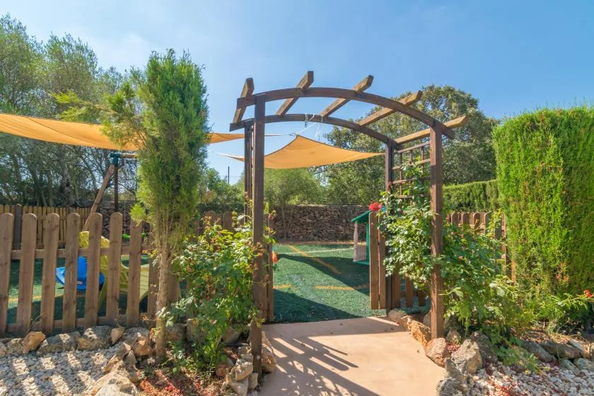 Un sendero de jardín pasa bajo una pérgola de madera hacia una zona verde al aire libre.