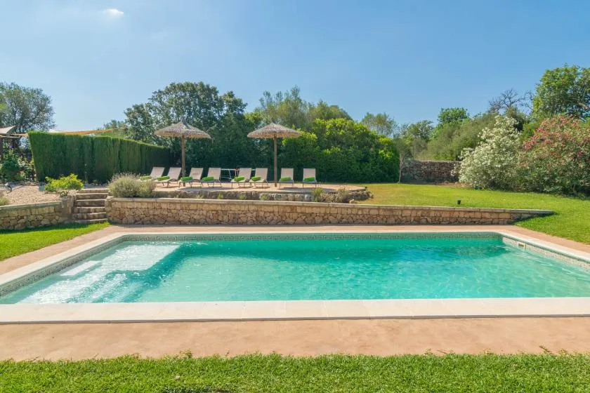Una piscina al aire libre junto a un césped y varias tumbonas.