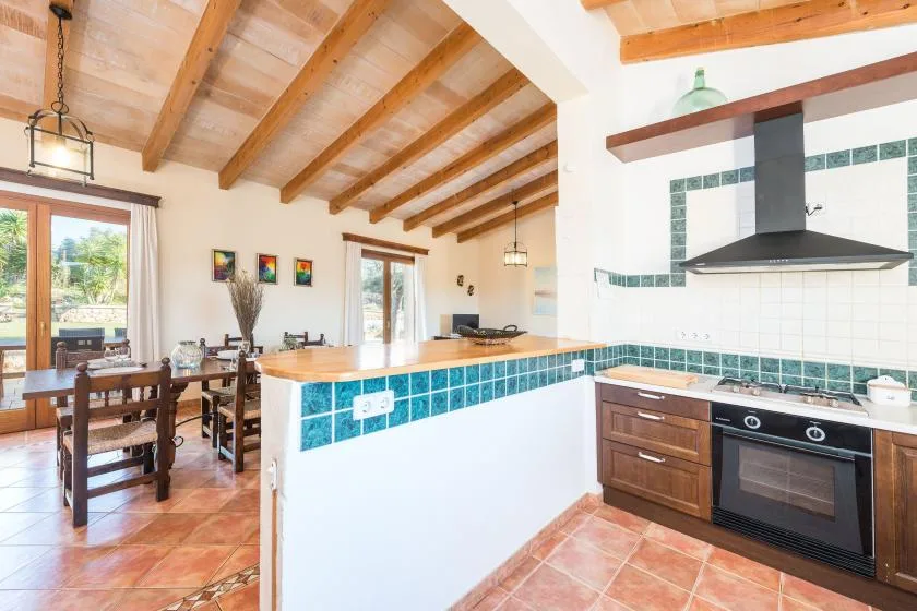 Una cocina y comedor con una isla revestida de azulejos, mesa de madera y vigas expuestas.