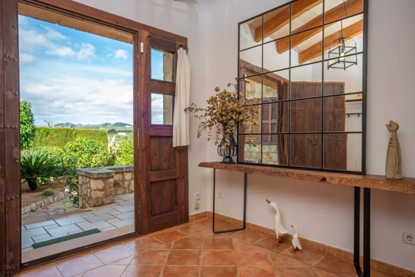 Una habitación con suelo de baldosas se abre al jardín por una puerta de madera, con una mesa consola junto a la pared.
