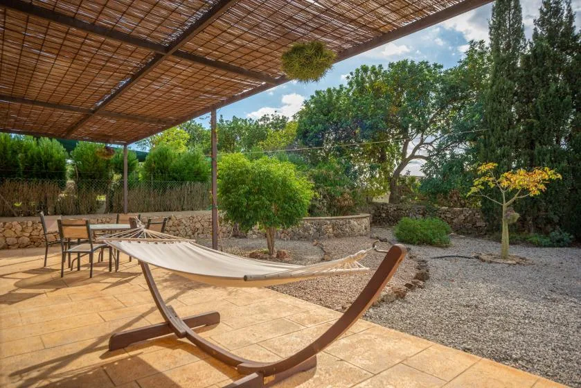 Un patio exterior sombreado con una hamaca, asientos y árboles alrededor.