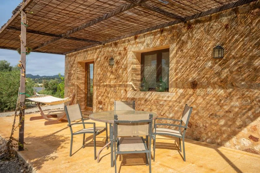Un patio exterior sombreado con una mesa y asientos junto a un muro de piedra.