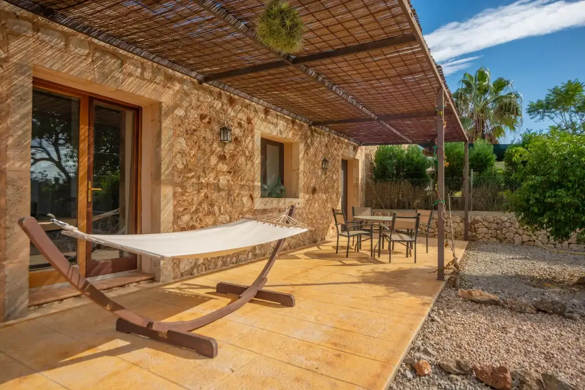 Un patio de piedra con una hamaca de tela bajo una pérgola sombreada.