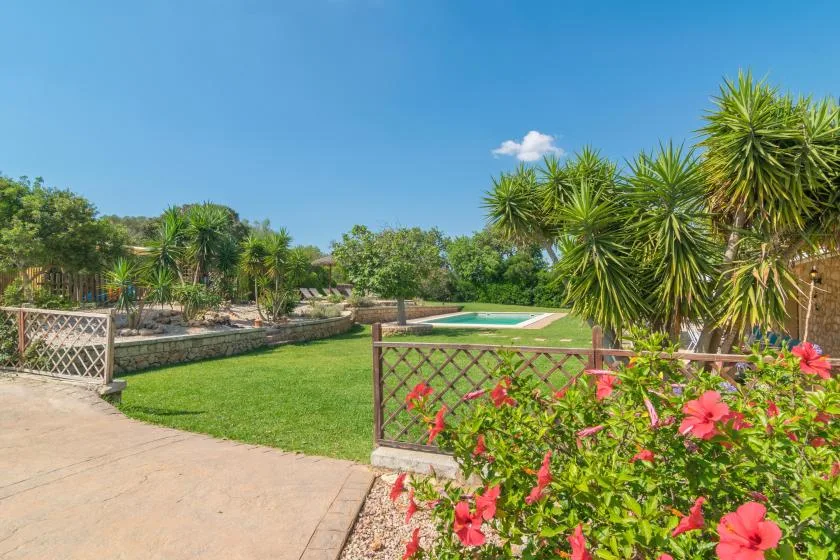 Un jardín ajardinado con piscina, césped verde y plantas con flores.