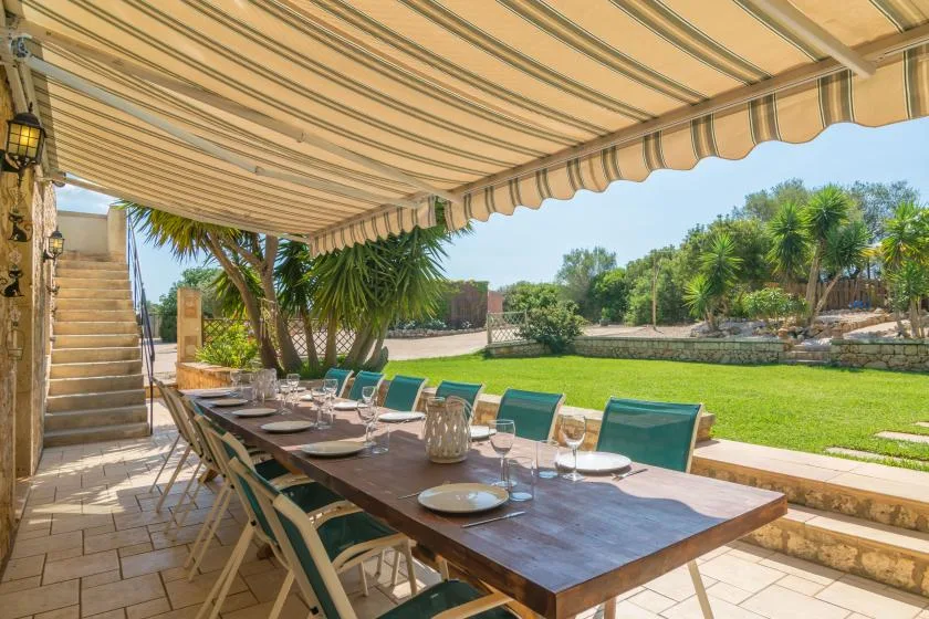 Una mesa de comedor al aire libre está bajo un toldo a rayas junto a un césped.