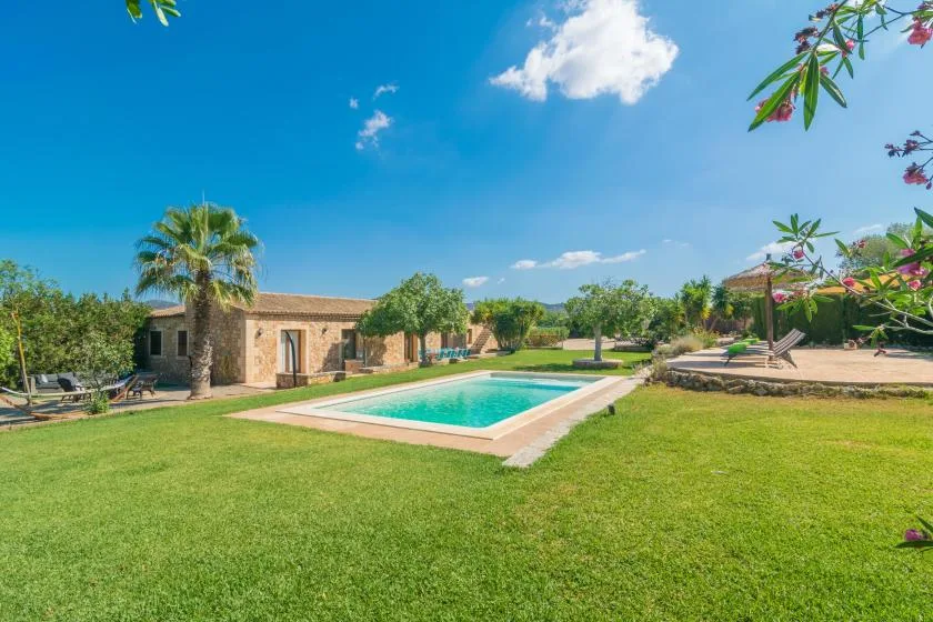 Una piscina está en un jardín de césped junto a un edificio bajo de piedra.