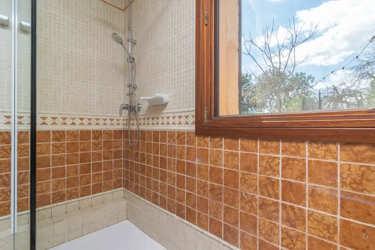 Un baño alicatado con ducha y una ventana con vistas a los árboles.
