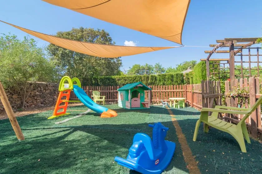 Un parque infantil al aire libre con tobogán, casita y zona de juegos sombreada.