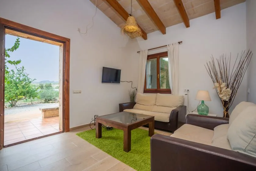 Una sala luminosa con asientos, una mesa de centro y una puerta abierta a un patio.