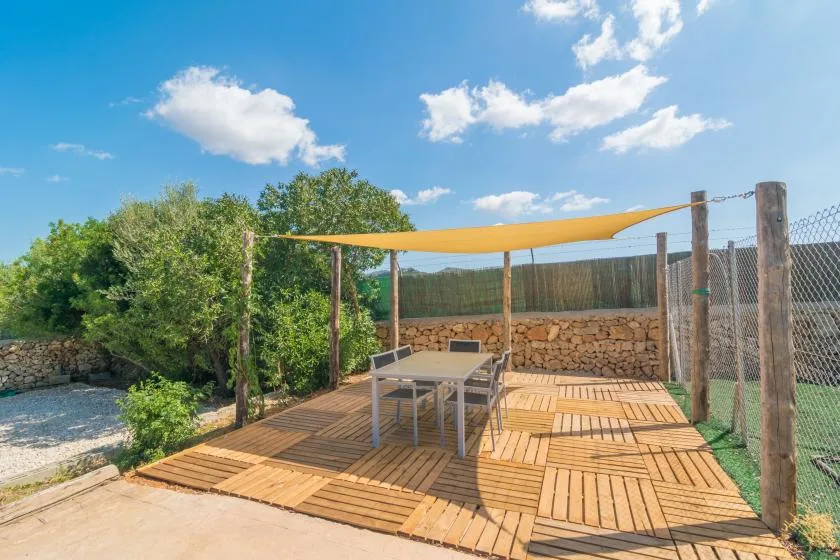 Una terraza exterior de madera con mesa y asientos bajo un toldo.