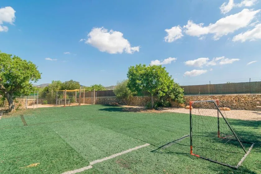 Una cancha exterior cercada con césped verde y una portería pequeña.