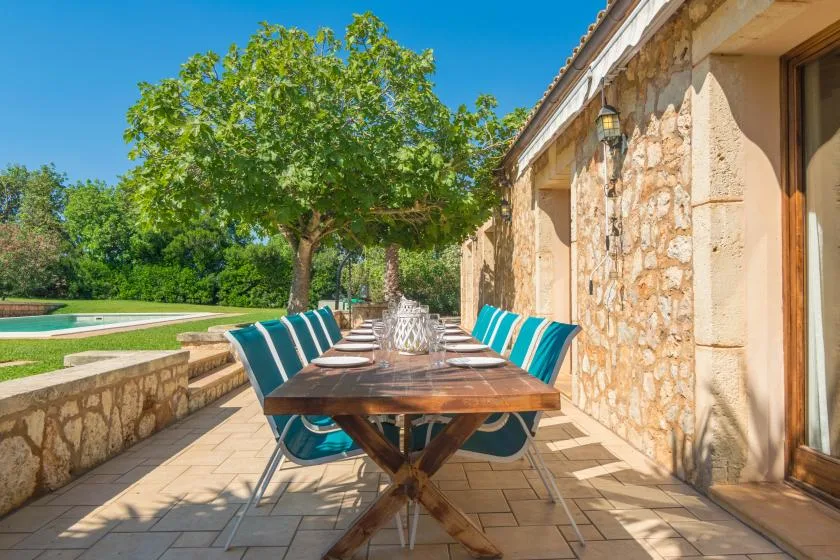 Comedor al aire libre con una mesa larga y asientos azules junto a un muro de piedra.