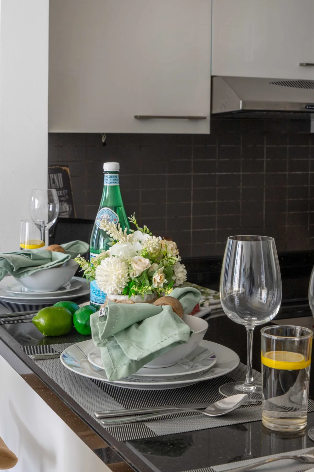 A kitchen counter is set with dishes, drinks, and a flower arrangement.