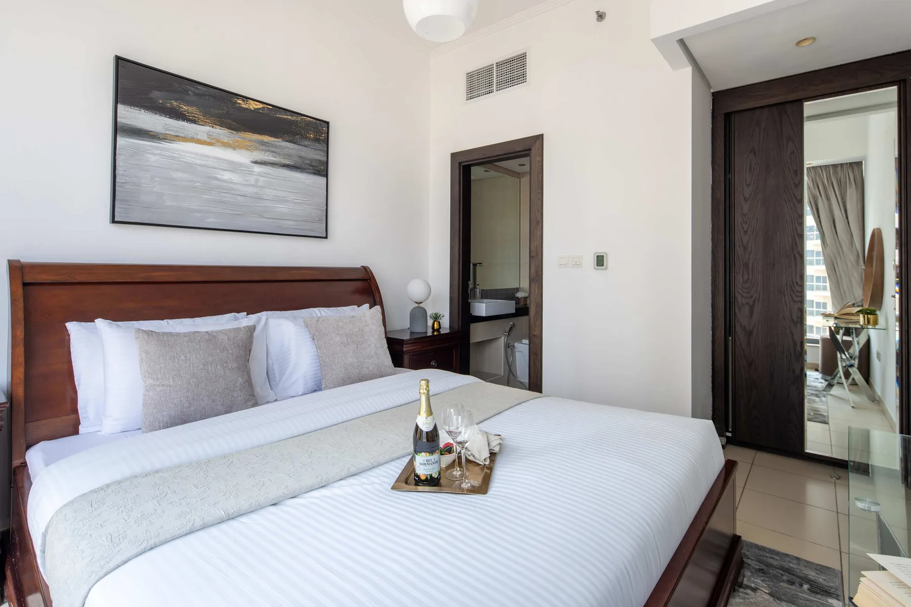 A bedroom with a neatly made bed, framed artwork, and a wardrobe.