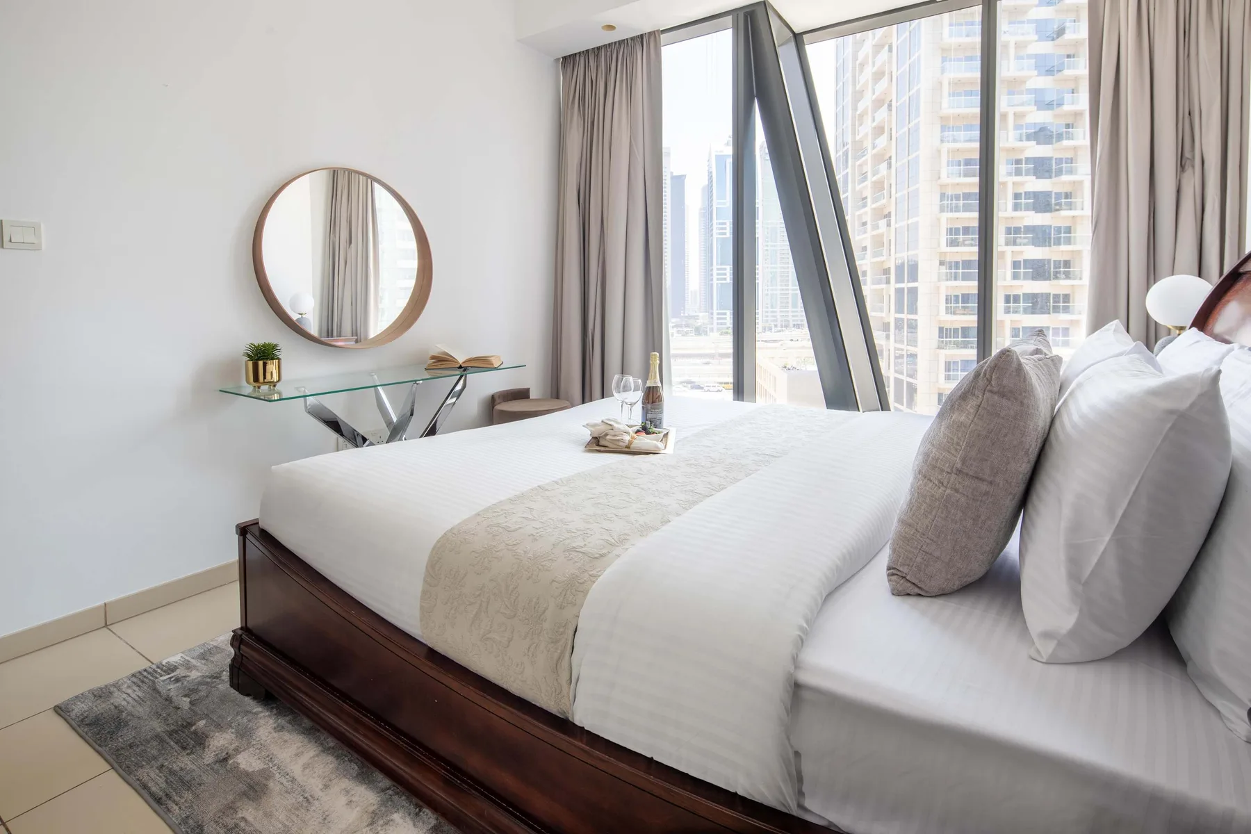 A bright bedroom with a neatly made bed beside floor-to-ceiling windows.