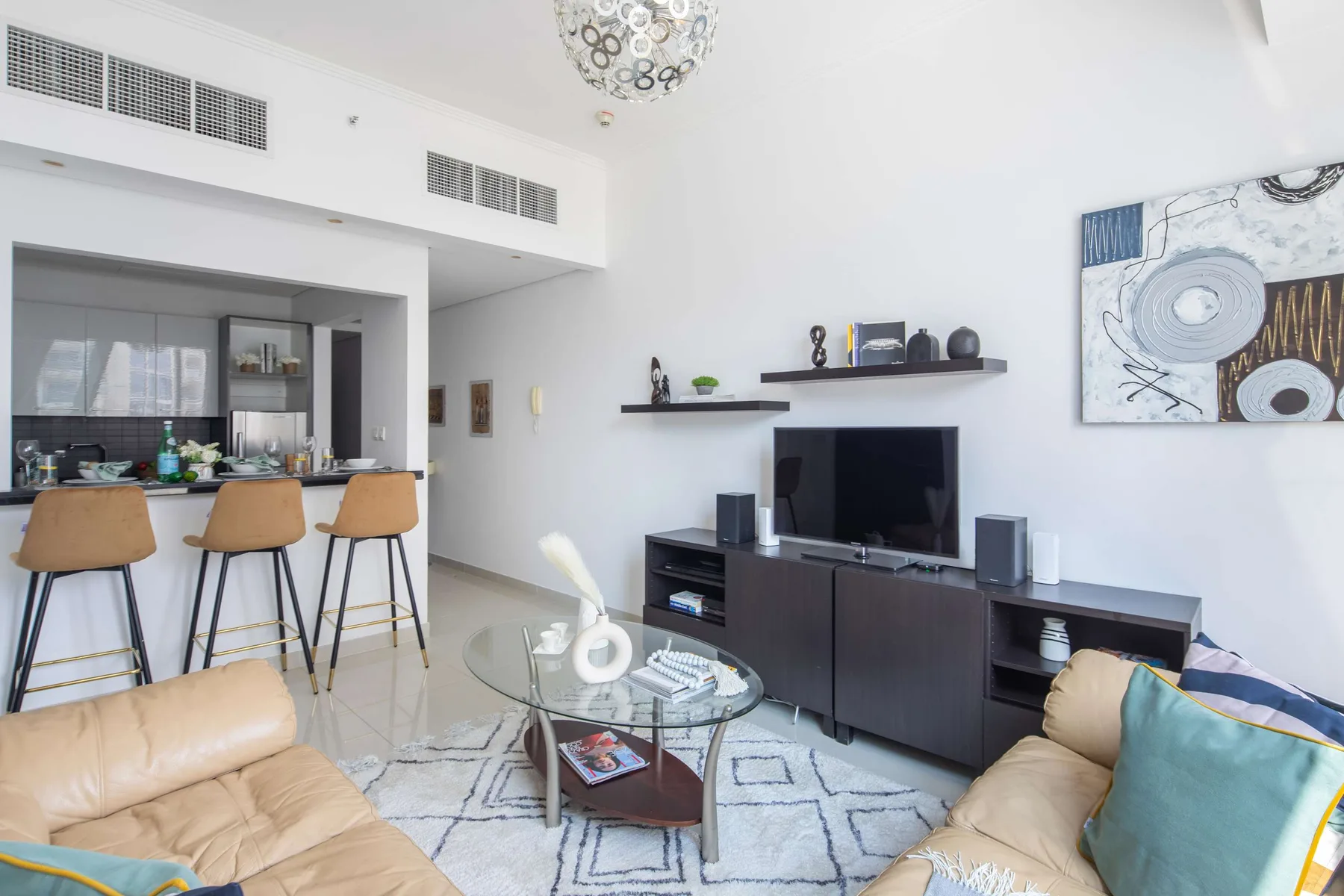 Una sala luminosa con asientos, un televisor y una cocina abierta.