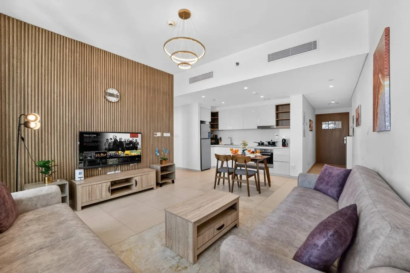 Sala de estar con asientos, un televisor y una cocina y comedor abiertos.