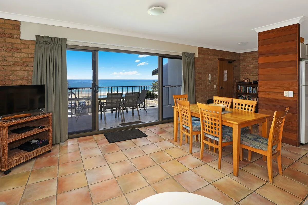 A dining area with wooden seating beside sliding glass doors opening onto a balcony.