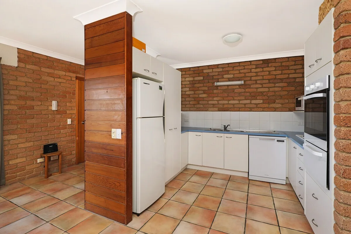 A brick-walled kitchen with white cabinets and tiled floors.
