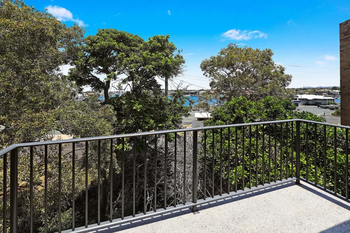 A balcony overlooks leafy trees and a distant waterfront.