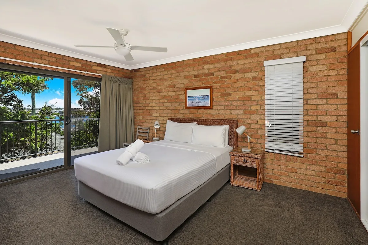 A bedroom with a bed beside a sliding glass door opening onto a balcony.